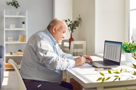 Old senior man working using laptop with chart sitting at the desk at home. Elderly retired person sitting at table and calculating finances, income and profit planning budget and checking bills.