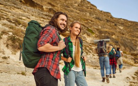 Man tourist and young girl hiking in nature with a group of tourists in mountains looking into the distance while trekking with backpacks. Travel, adventure and people tourism concept.