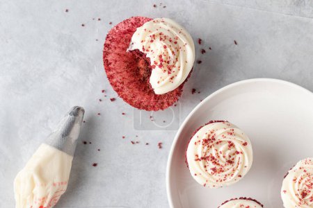 Photo for A half eaten red velvet cupcake with a piping bag on a light background - Royalty Free Image