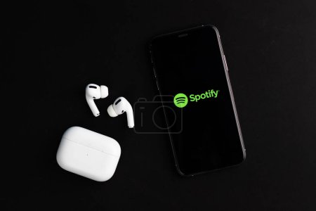 Foto de Logo de Spotify mostrado en la pantalla del teléfono con Airpods Pro en el escritorio - Imagen libre de derechos
