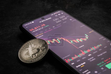 Photo for Bitcoin price and graph opened in binance with a silver bitcoin on a dark background - Royalty Free Image