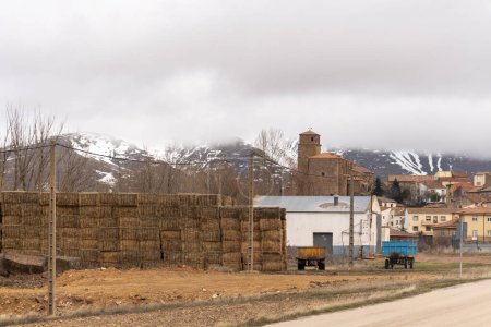 Photo for Discover the breathtaking beauty of Borobia, Soria with this stunning panoramic photograph featuring snow-capped Moncayo mountain and charming alpaca haystacks in the foreground. Two tractors add a touch of rustic charm to this picturesque landscape, - Royalty Free Image
