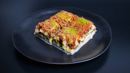Photo for Cold baklava with pistachios, a traditional Turkish delicacy, presented with a black background and a dark plate. - Royalty Free Image