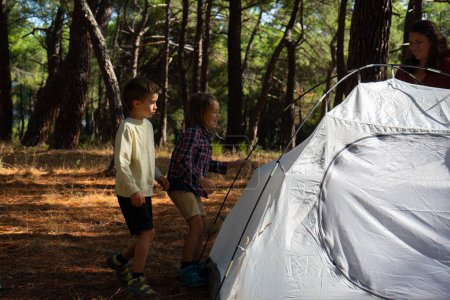Two children pitching a tent together in the woods