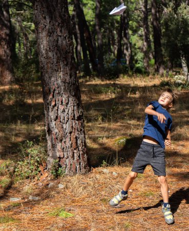 Photo for Boy launching a paper airplane into the forest - Royalty Free Image