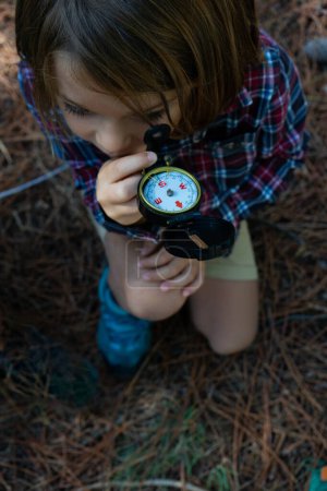 Photo for Child looking at a compass in the forest seen from above - Royalty Free Image