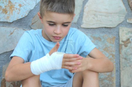 Sitzendes Kind blickt auf seine bandagierte Hand
