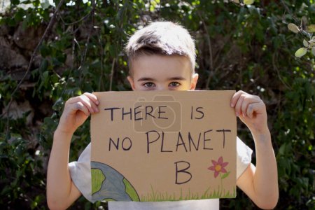 Foto de Niño sosteniendo el letrero "No hay planeta B" mirando a la cámara - Imagen libre de derechos