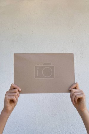 Téléchargez les photos : Affiche en carton clair tenue par les mains d'une femme avec un mur blanc en arrière-plan - en image libre de droit
