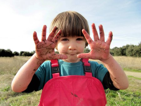 Kleiner Junge in der Natur zeigt seine Hände voller Schlamm
