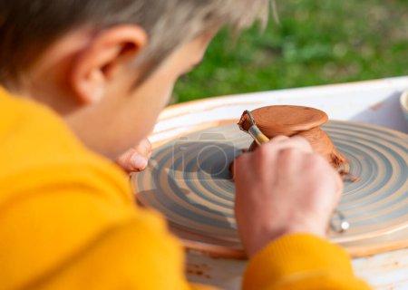 Boy learning to use potter's wheel outdoors