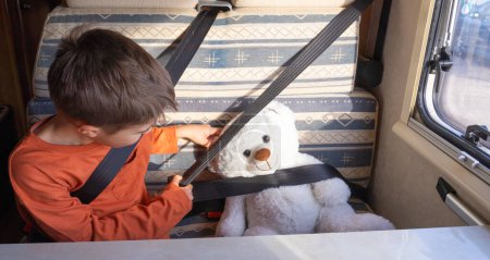 Boy fastening the seat belt to his white teddy bear