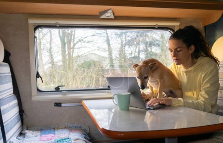 Photo for Woman teleworking with a computer from a motorhome with her dog - Royalty Free Image