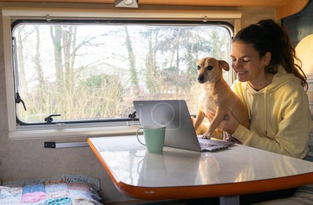 Photo for Woman working remotely with a laptop inside a motorhome with her dog - Royalty Free Image