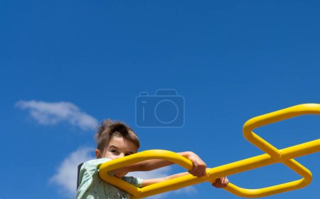 Téléchargez les photos : Garçon escalade une structure dans un parc avec un fond bleu ciel - en image libre de droit
