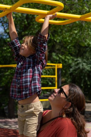 Junge klettert mit Hilfe seiner Mutter eine Parkstruktur hinauf