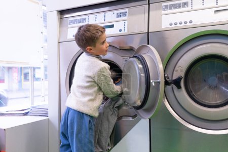 Kaukasischer Junge stellt eine Waschmaschine in einen Waschsalon, um Wäsche zu waschen