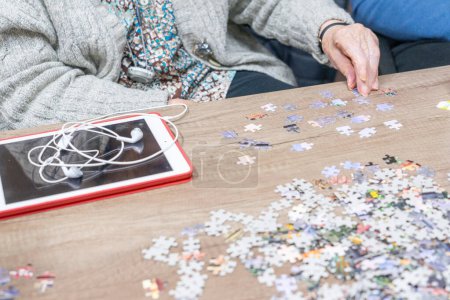 Elderly woman's hand doing a puzzle and a tablet at the table