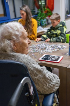 Elderly woman in a nursing home receiving a visit from her granddaughter and great-grandson