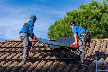 Photo for Two solar panel installers installing solar panels on the roof of a house - Royalty Free Image