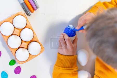 Niño pintando un huevo de Pascua azul con marcador visto desde arriba
