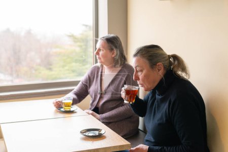 Two older women friends drinking tea together in a cafe