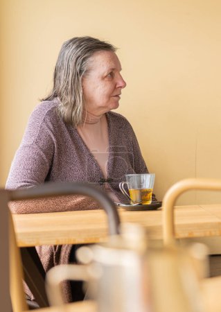 Seniorin in einem Café trinkt Tee mit Pfirsichhintergrund