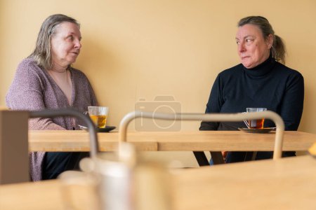 Zwei ältere Freunde beim gemeinsamen Aufguss in einem pfirsichfarbenen Café