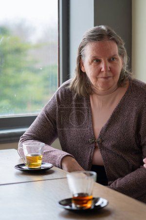 65-jährige Frau sitzt in einem Café und trinkt Tee