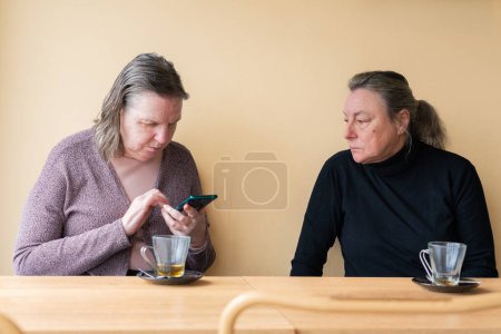 Two older women in a cafe, one looking at her cell phone