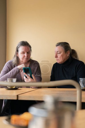 Seniorinnen schauen gemeinsam in Konditorei auf Handys