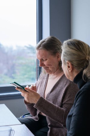 Zwei 60-jährige Freundinnen zusammen, eine schaut auf ihr Handy