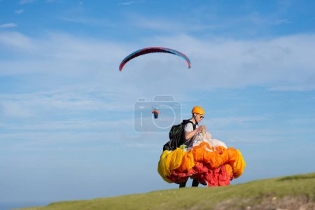 Man with the paraglider folded in cauliflower and another paraglider flying behind