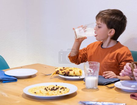 Junge frühstückt, trinkt ein Glas Milch und isst einen Pfannkuchen