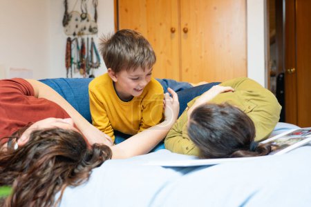 Boy playing with his two mothers in bed