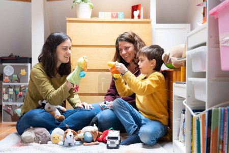 LGBT-Familie mit zwei Müttern und ihrem Sohn, die zusammen im Zimmer mit Kinderspielzeug spielen