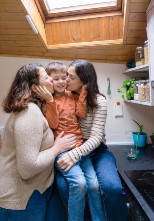 Boy with his two mothers giving him a kiss in the kitchen of their house. LGBT family