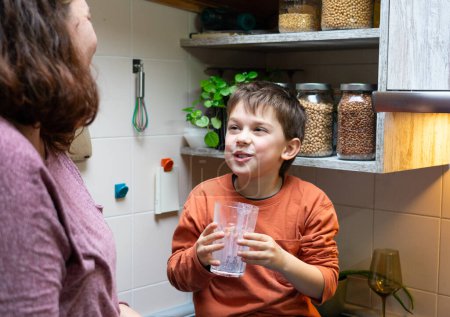 Joyeux garçon buvant un verre de lait dans la cuisine à la maison avec sa mère
