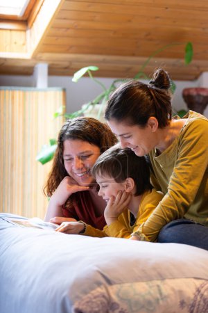 Familia LGBT de dos madres felices y su hijo mirando un álbum de fotos juntos en casa