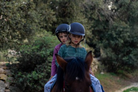 Two children riding horses together in the field