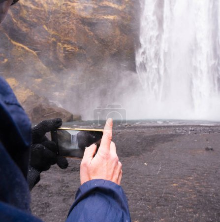 Mann macht ein Foto mit seinem Handy am Wasserfall