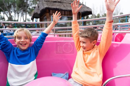 Dos niños caucásicos de 8 años se divierten en el paseo de la taza en un parque de atracciones.
