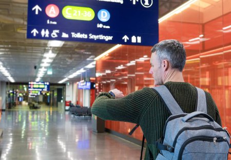 Moyen homme voyageur caucasien d'âge à l'aéroport regardant horloge