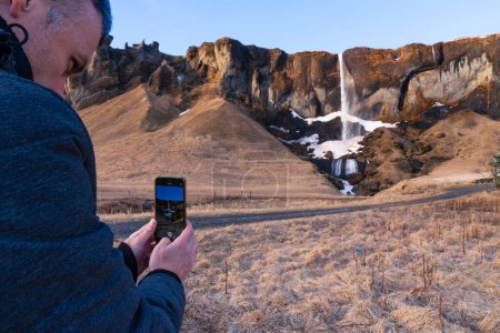 Man taking a photo with his cell phone of a waterfall in Iceland
