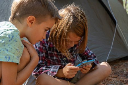 Kinder zelten im Wald und spielen mit Smartphone