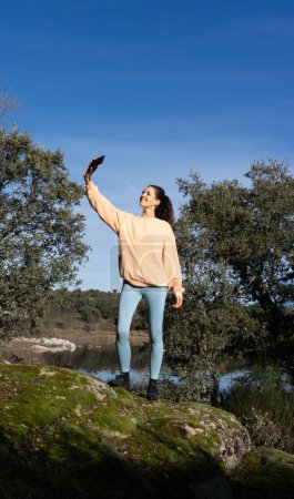 Frau macht ein Selfie mit ihrem Handy in der Natur in Pfirsichfarbe