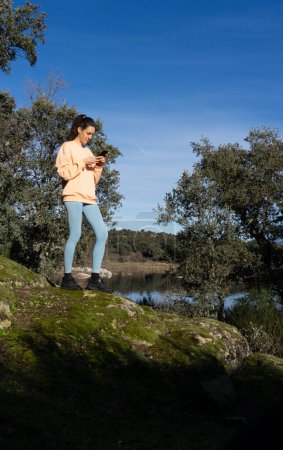 Mujer deportiva mirando el teléfono celular en la naturaleza