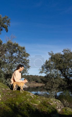 Frau sitzt mit Hund in der Natur