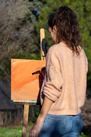 Photo for Woman painting on a canvas with peach fuzz color paint abstract art in nature - Royalty Free Image