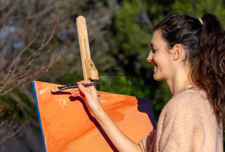 woman happily painting a canvas with peach-colored paint outdoors